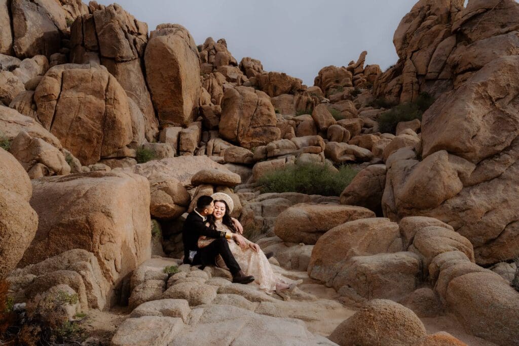 Couple sitting on boulders at Cap Rock surrounded by jumbo rocks during their Joshua Tree adventure elopement