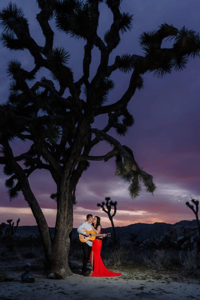 Couple eloping in Hidden Valley during golden hour, playing guitar under a Joshua tree at sunset