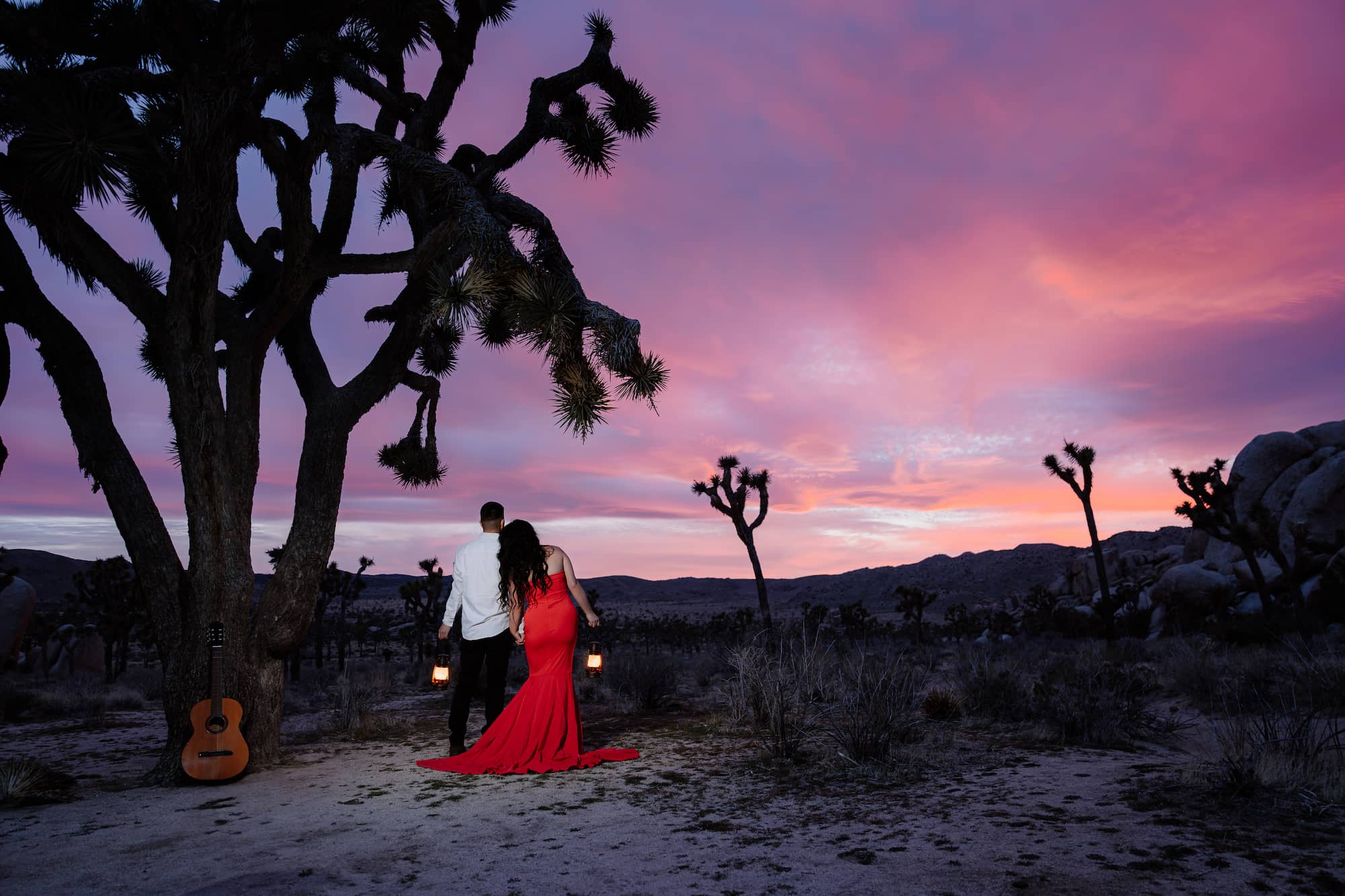 Couple walking with lanterns at sunset in Joshua Tree’s Hidden Valley — elopement by colorful vibrant photographer