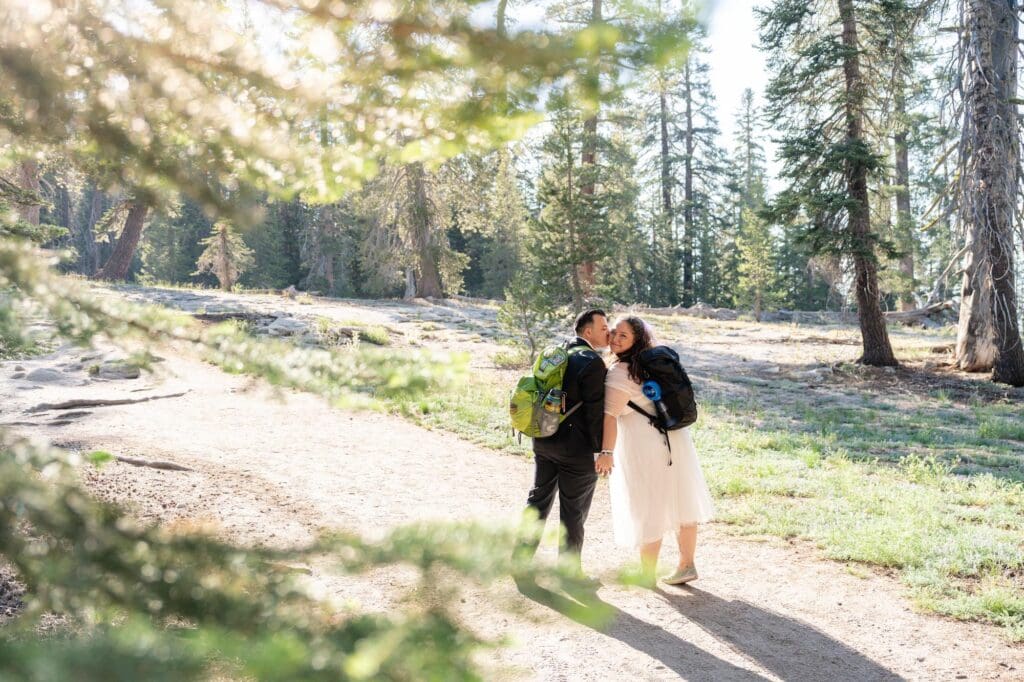 How to Elope in Yosemite – Forest Trail Moment Couple hiking through the forest trail for their Yosemite elopement, holding hands and smiling in the trees.