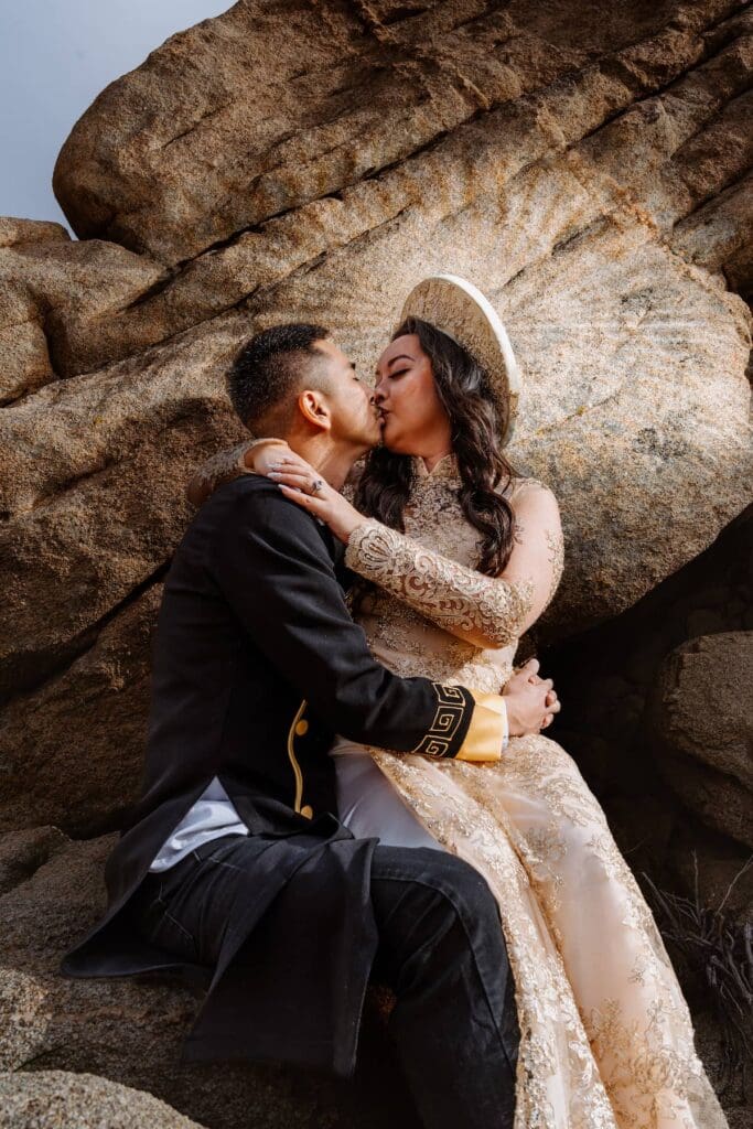 Couple in embroidered Ao Dai sharing a kiss at Cap Rock during their intimate elopement in Joshua Tree
