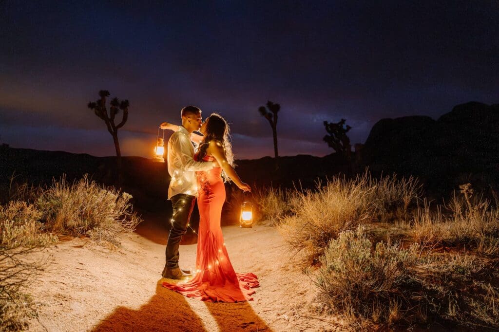 Couple sharing a kiss wrapped in lanterns and lights during their vibrant blue hour elopement in Joshua Tree