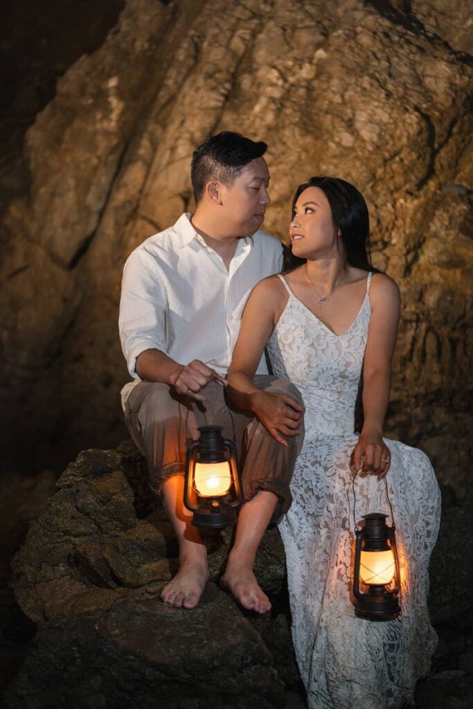 Elopement couple sitting on rocks inside the cave holding lanterns at El Matador State Beach