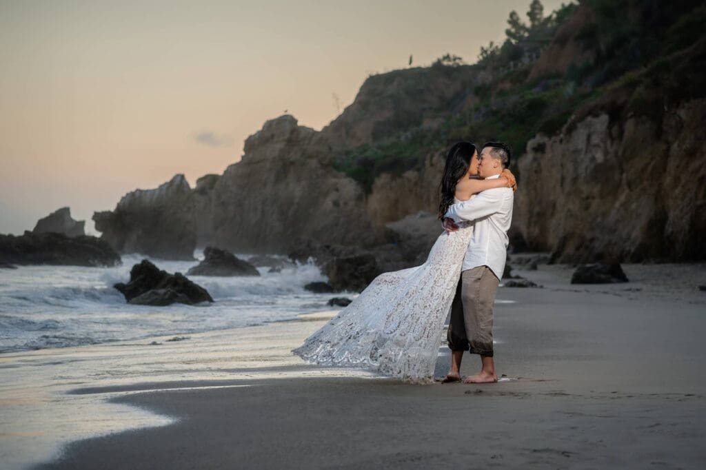 Bride and groom kissing on the sand with golden cliffs behind them at El Matador Beach