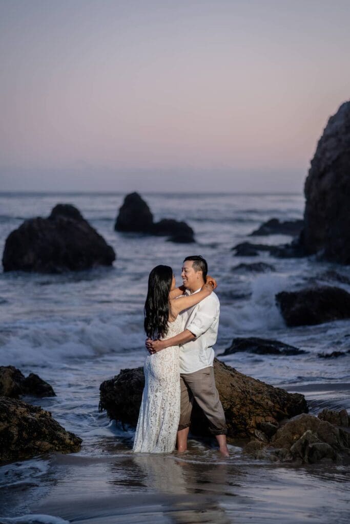 Couple embracing on the rocky shoreline at El Matador State Beach during their romantic Malibu elopement at blue hour