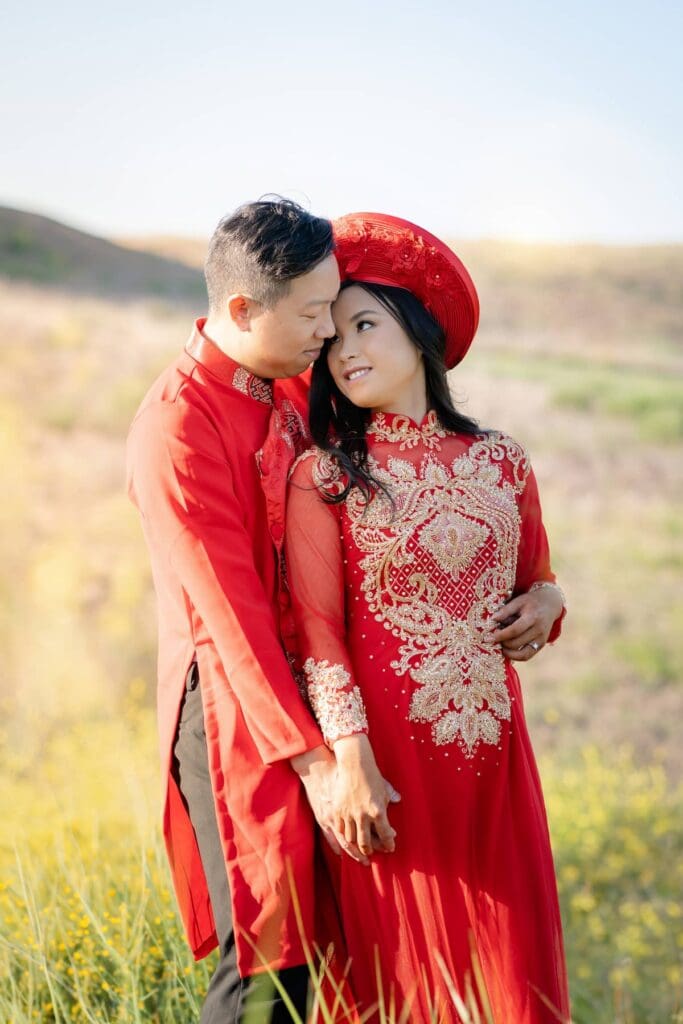 Couple embracing in red traditional Vietnamese wedding attire at Malibu State Park wildflower field