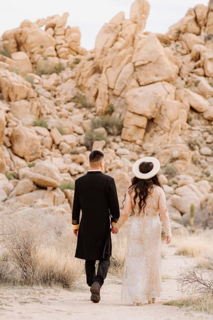 Bride and groom walking toward desert rocks holding hands.