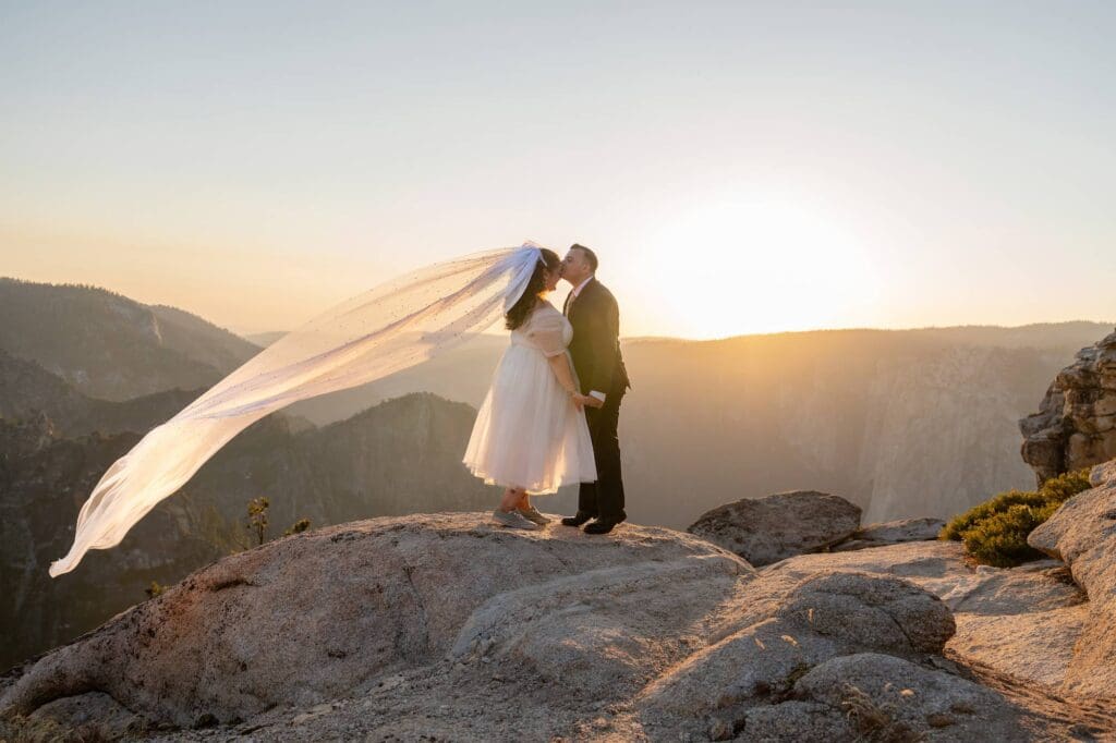Morgan and Jesse kiss during their Yosemite elopement as her veil flows in the wind at Taft Point