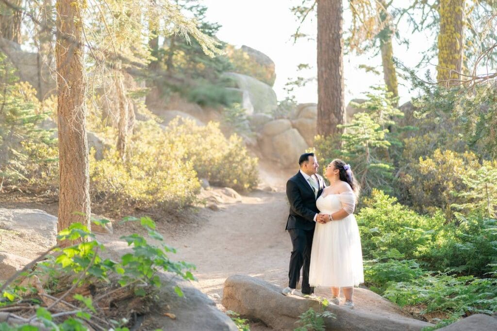 Couple standing in the forest trail with golden light shining through the trees