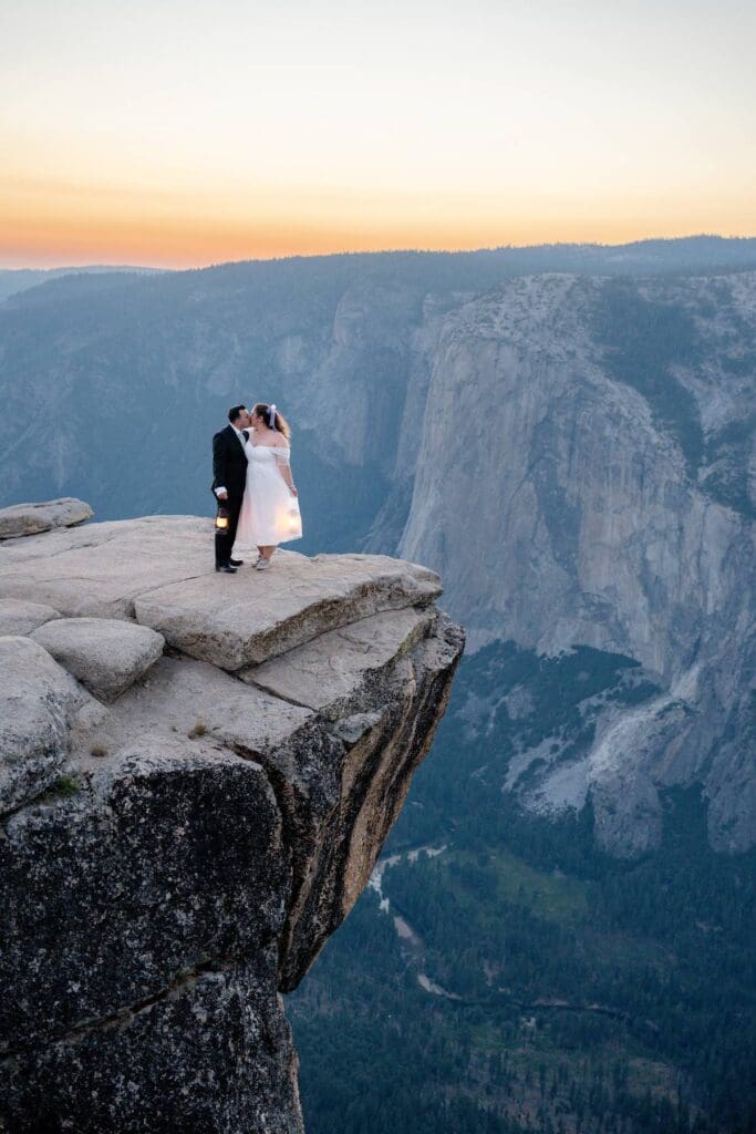 Couple kissing on a cliff at Taft Point with lanterns during their Yosemite elopement at sunset